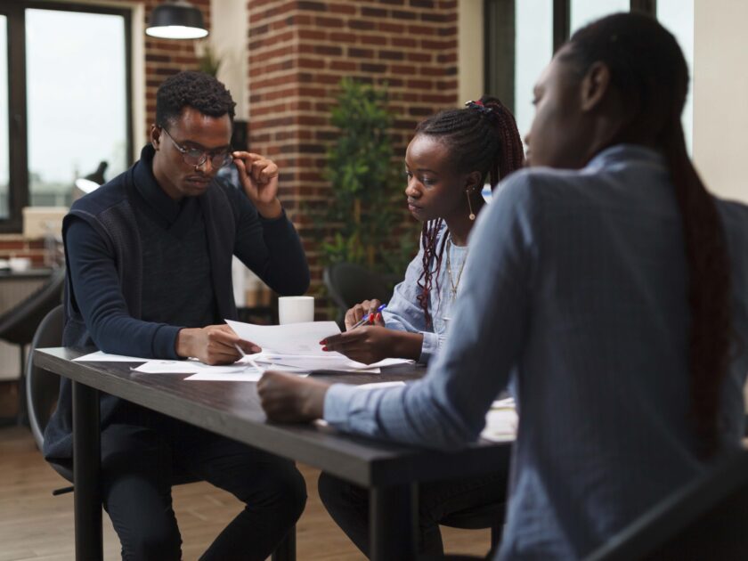 African american research agency coworkers in meeting about startup project financial status. Business people at desk in company office finance department talking about marketing expenses.